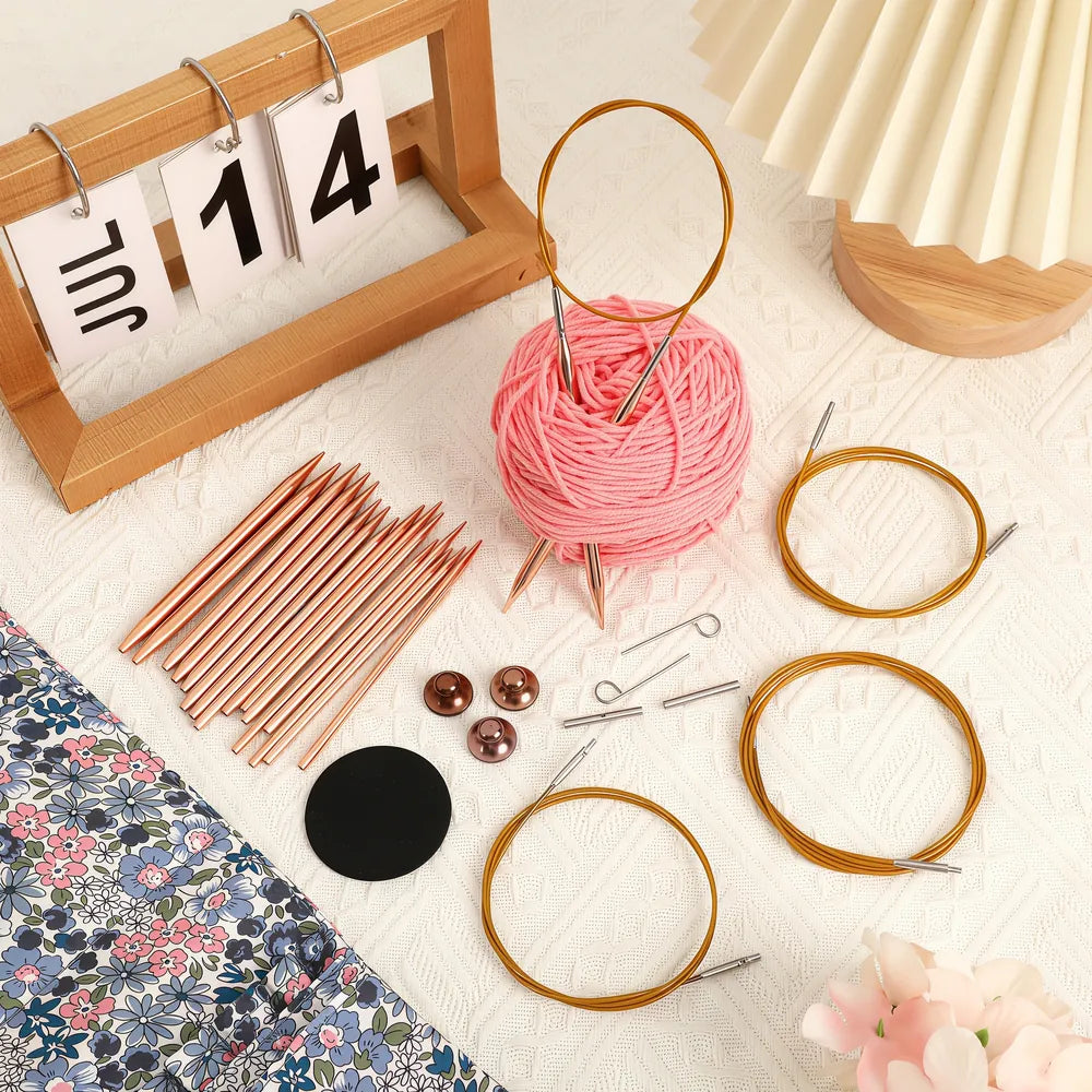Rose gold circular knitting needle set displayed with pink yarn and floral pouch