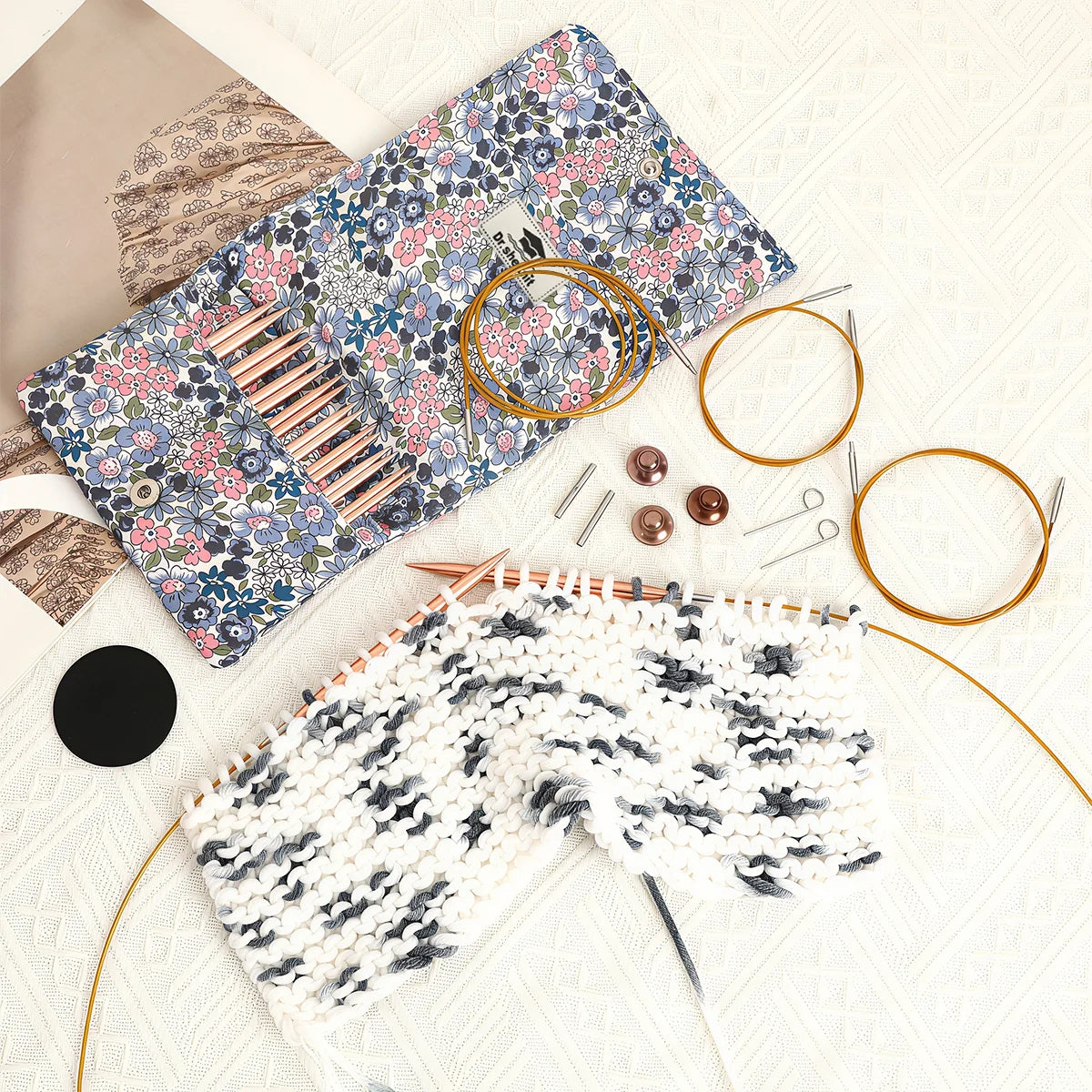 Rose gold interchangeable circular knitting needles in use with floral pouch and accessories nearby